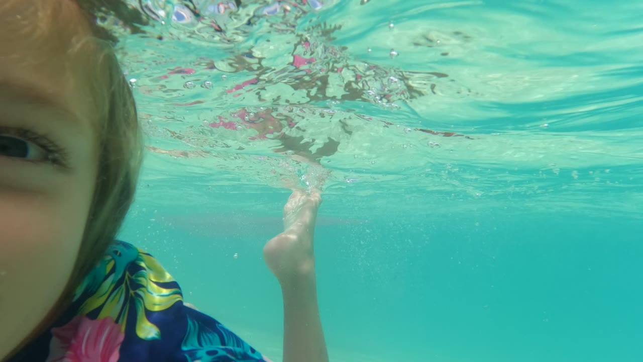 Underwater frame in Baja California, Mexico with half of the child's face close to the left edge, one arm in the water, and rippled turquoise surface light above.