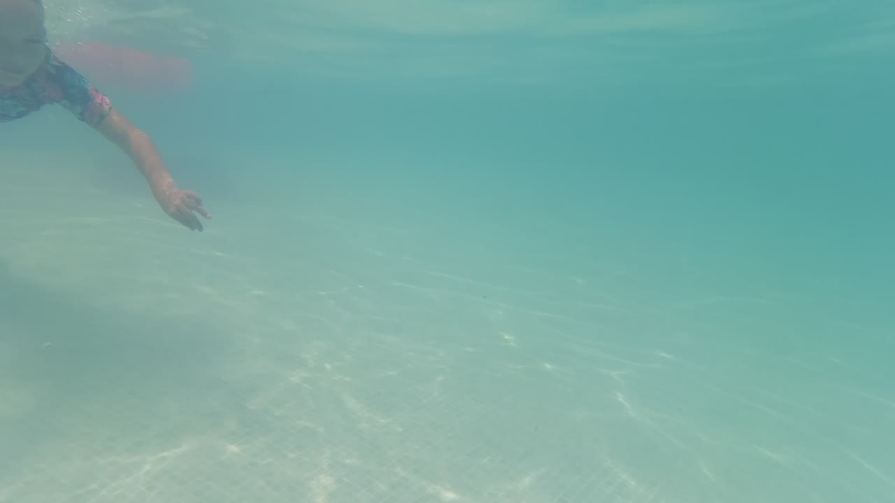 At 0:00 in Baja California, Mexico, part of a child enters from the upper left underwater, with an arm reaching across clear turquoise water over rippled sand.