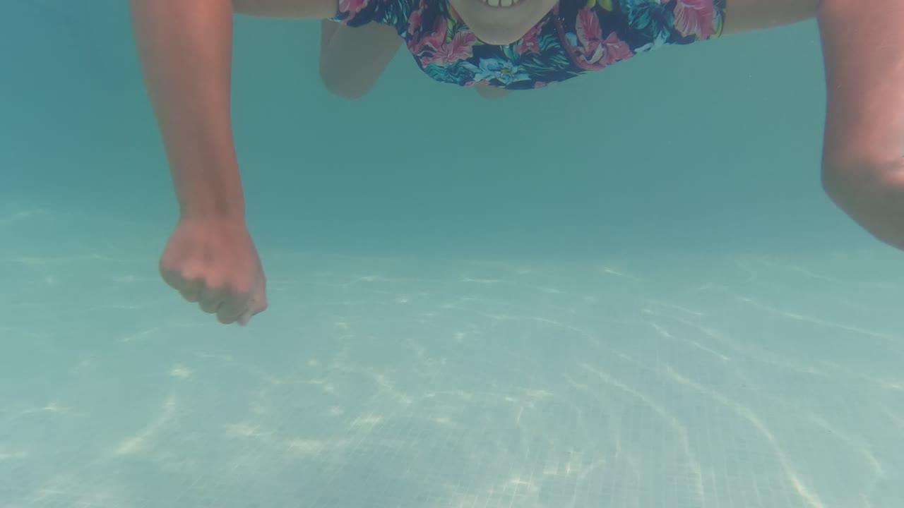 A close underwater frame in a Baja California, Mexico pool shows the child's arm, floral swim shirt, and part of the body near the water surface.
