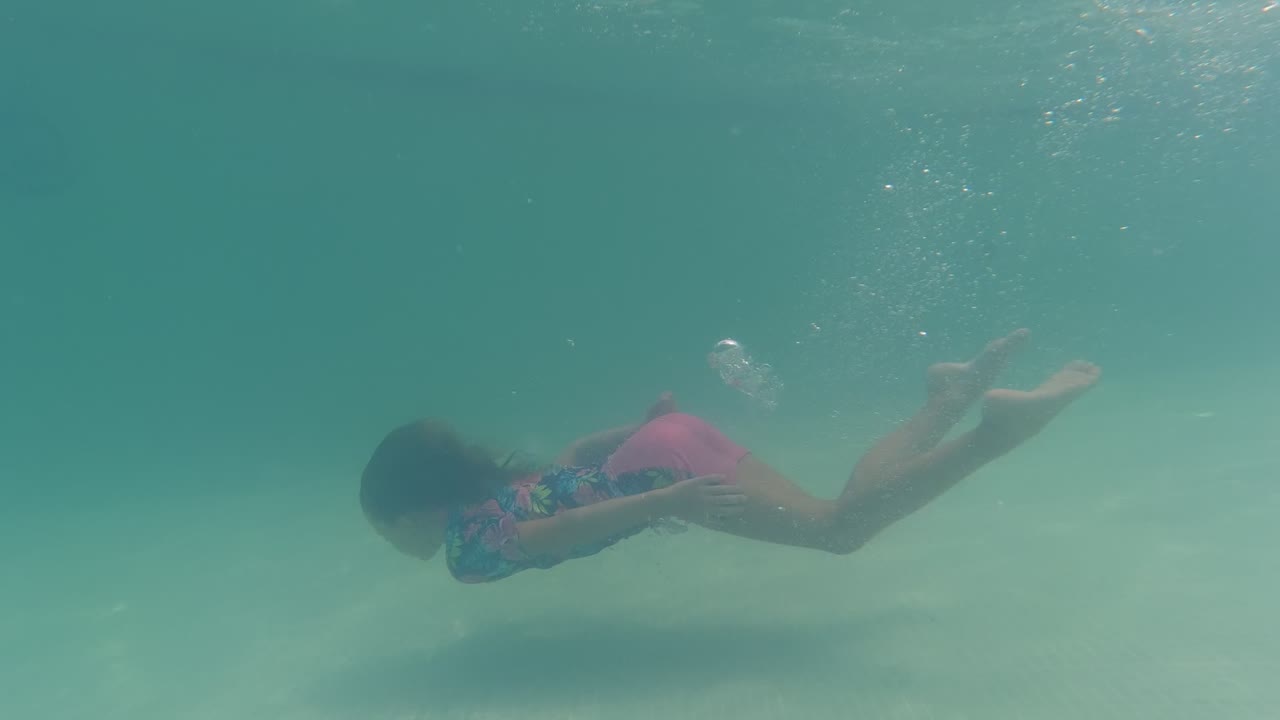 Girl gliding underwater with legs extended behind her.
