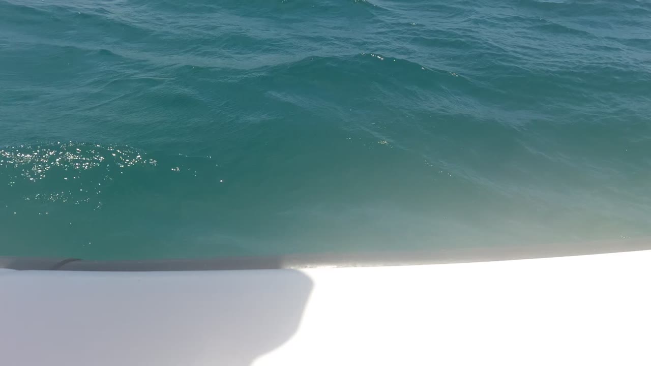 Blue-green ocean fills the view beside a white boat edge in Baja California, Mexico, with bright sun on the water and no visible people.