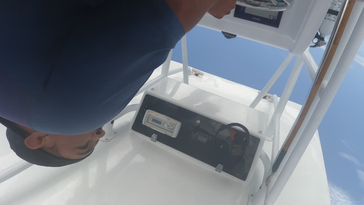 In Baja California, Mexico, a man in a dark blue shirt and cap leans into the top of the frame above a white boat console with a steering wheel and electronic display.