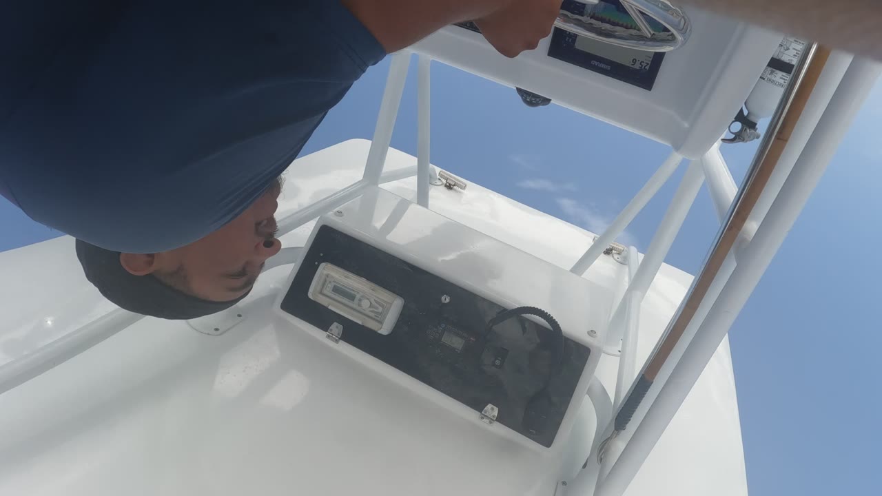 In Baja California, Mexico, the tilted close view shows the man above the console, a steering wheel on the black panel, bright white boat surfaces, blue sky, and a small edge of ocean.