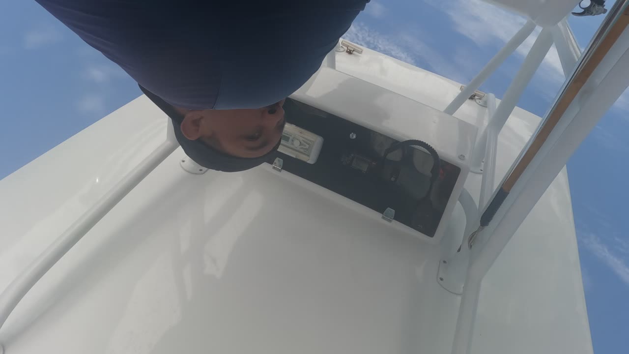 Person leaning near a black boat console with sky behind the white deck structure.