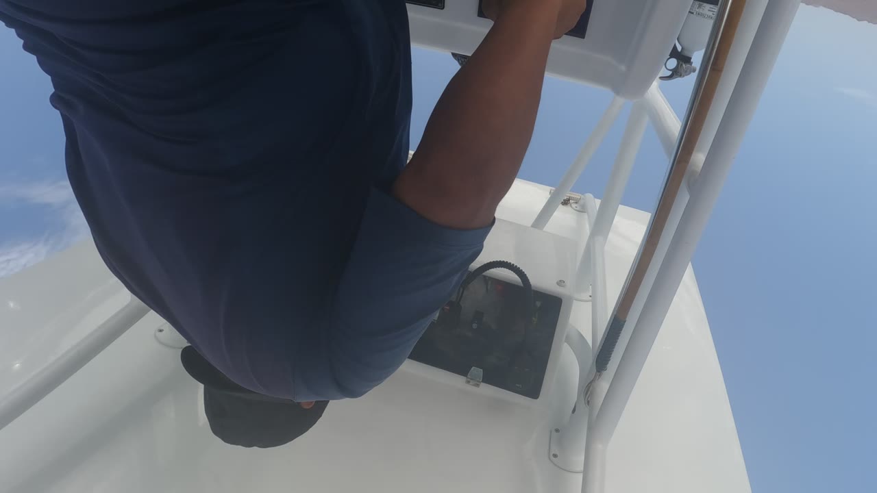 In Baja California, Mexico, a man in a blue shirt leans over a white boat console with railings and clear sky behind him at the start of the clip.