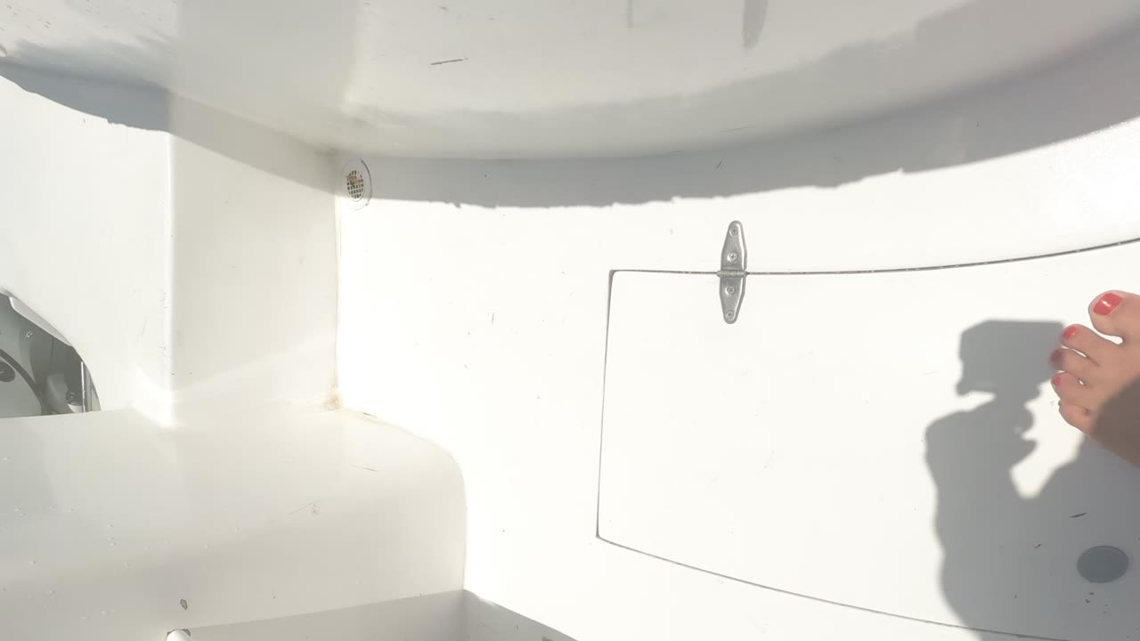 Bright white boat deck with a bare foot and camera shadow.