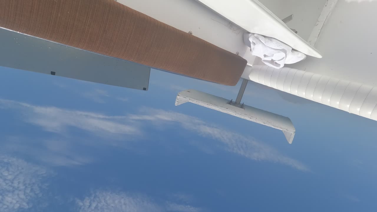 Aircraft wing above thin clouds in blue sky.