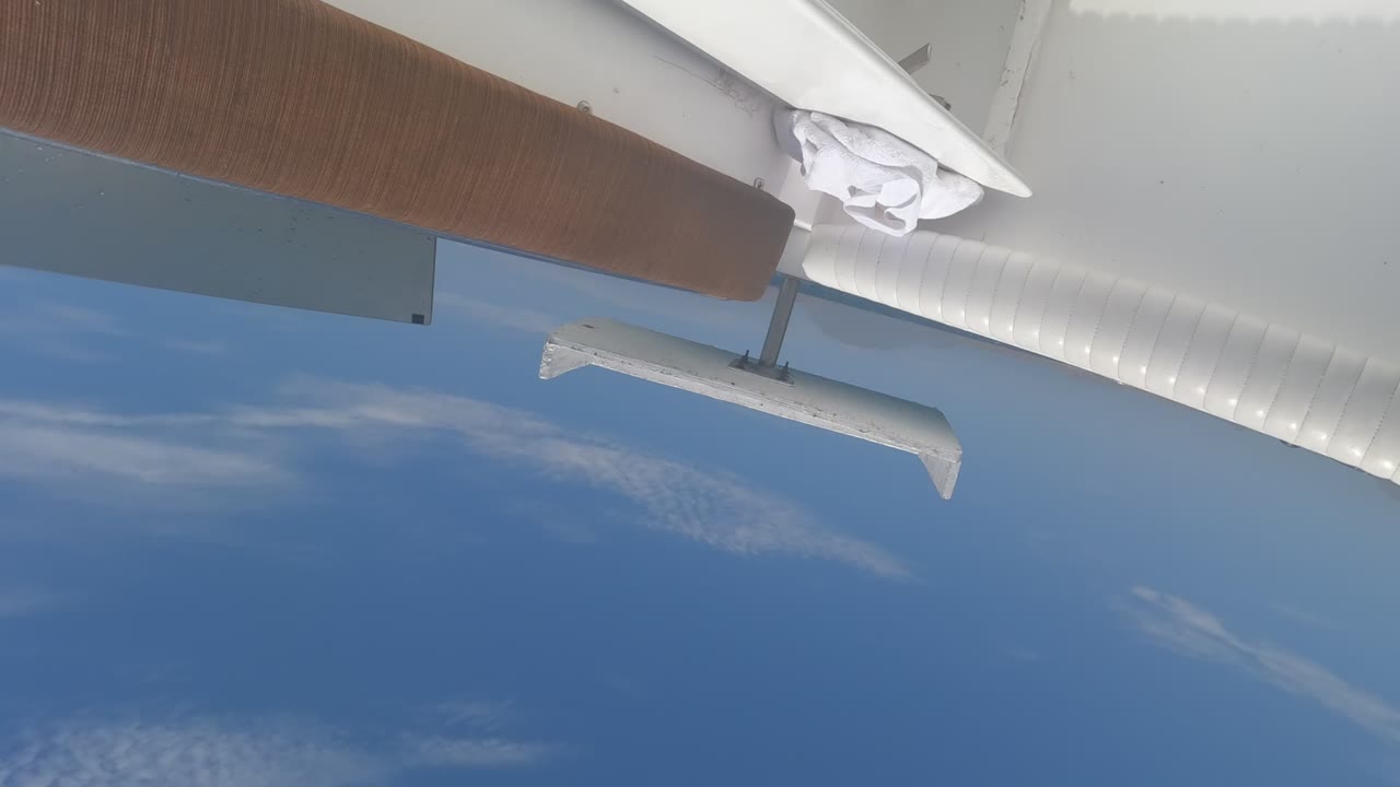 Baja California, Mexico in-flight frame with a white wingtip and strut against deeper blue sky and broken cloud streaks, no visible people.