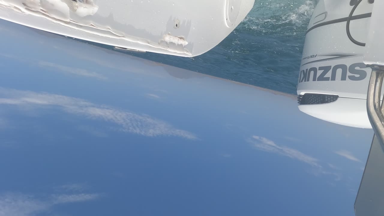At 0:02, the Suzuki outboard reappears along the right side of the tilted boat-mounted view, with the white hull, blue sea, and cloud streaks behind it in Baja California, Mexico, with no visible people.