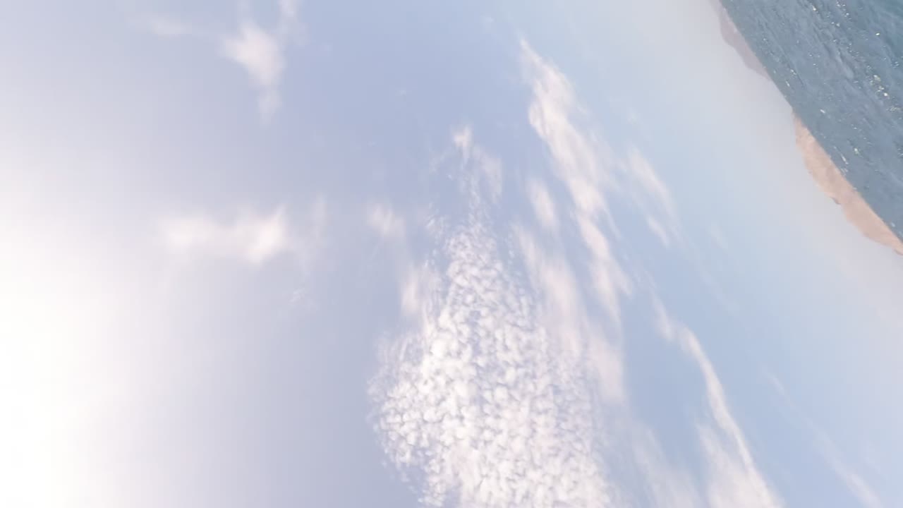 Bright sun glare fills the lower frame over blue sky and white clouds in Baja California, Mexico, with no visible people.