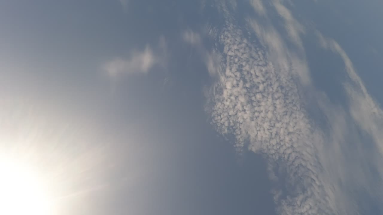 Sun glare sits low in a rotated sky view with a textured band of white clouds over Baja California, Mexico, and no visible people.