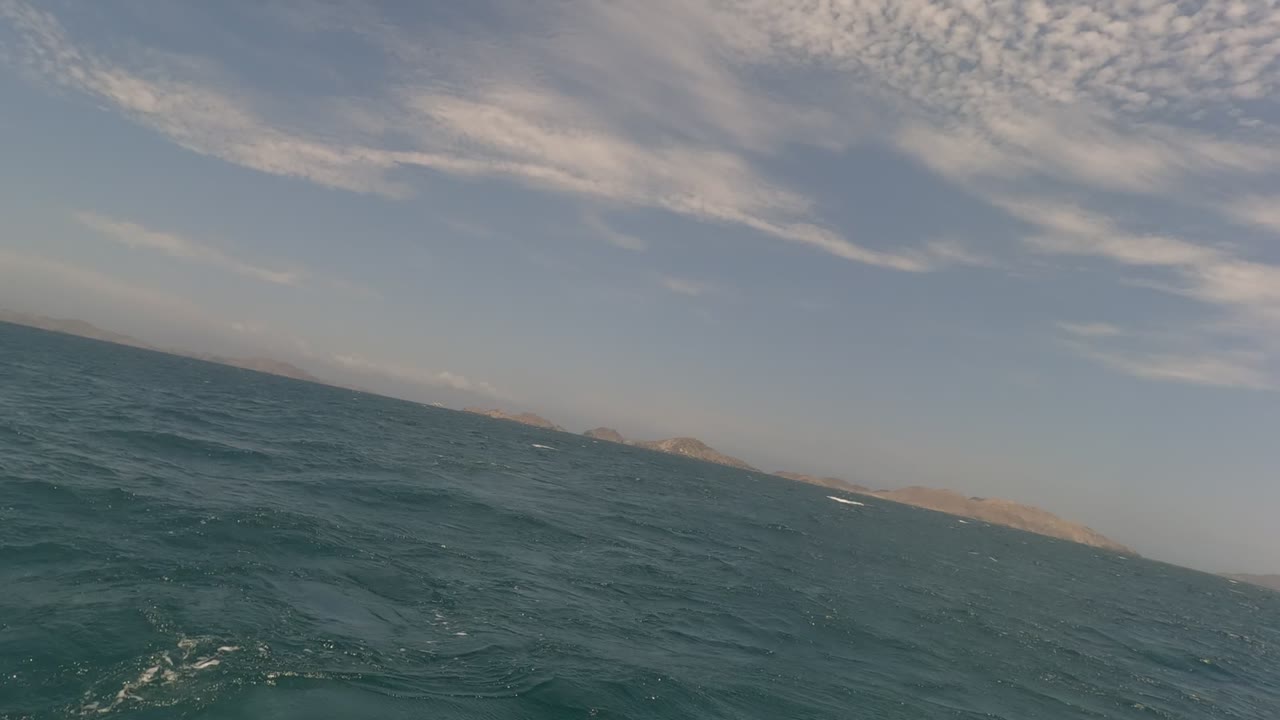Baja California ocean with choppy blue-green water, a tilted horizon, distant landforms, streaked clouds, and no visible people at 0:02.