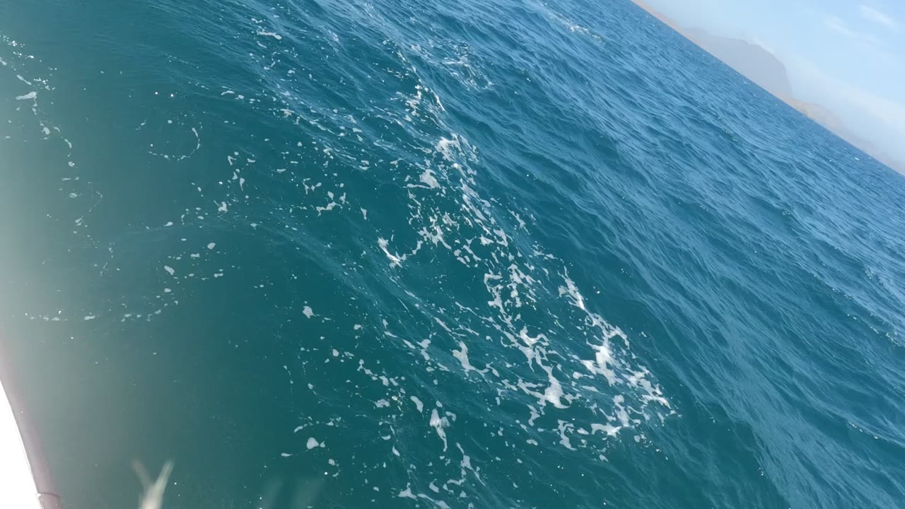 Tilted onboard view of blue-green ocean in Baja California Mexico, with small whitecaps and a pale boat edge at the left, no visible people.