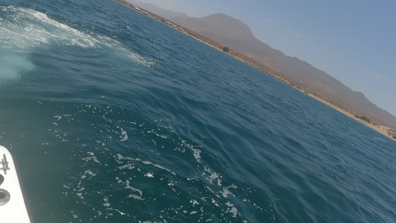 Ocean surface with foam, boat edge, sandy shore, and mountains
