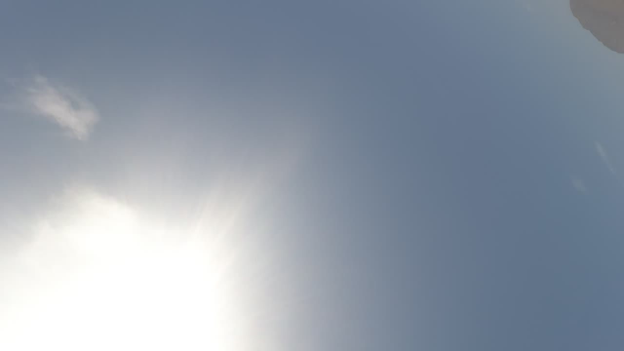 At 0:02 in Baja California, Mexico, the camera faces the bright sun in a blue sky with lens glare and a dark rounded obstruction near the upper right corner, with no visible people.