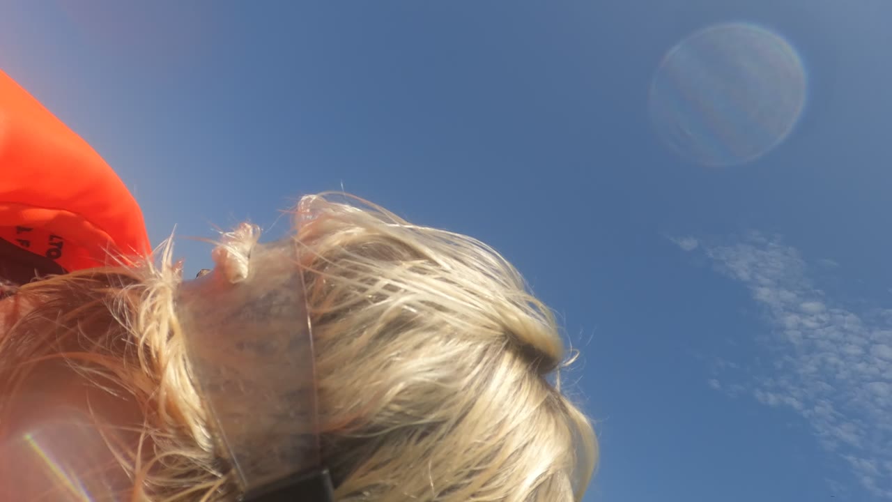Close-up in Baja California, Mexico of a blonde person partly out of frame with a snorkel strap and orange life jacket against a clear blue sky.
