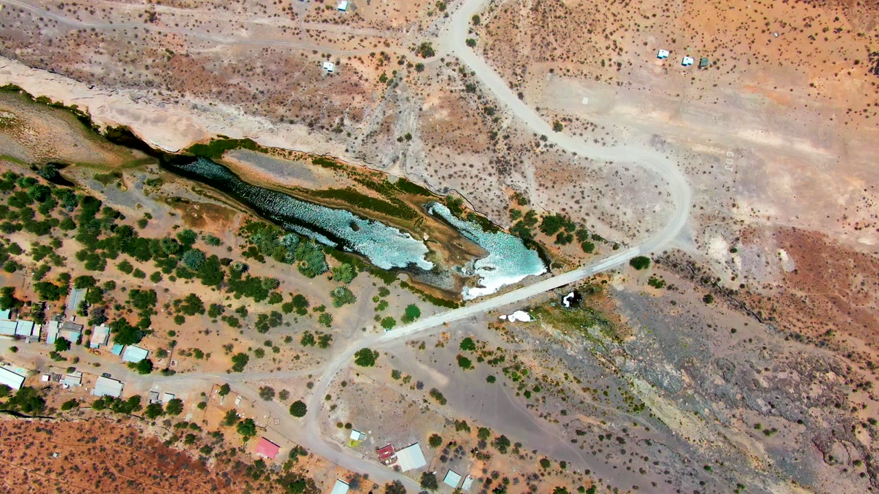 Aerial view of winding dirt tracks, desert scrub, and a narrow water body.