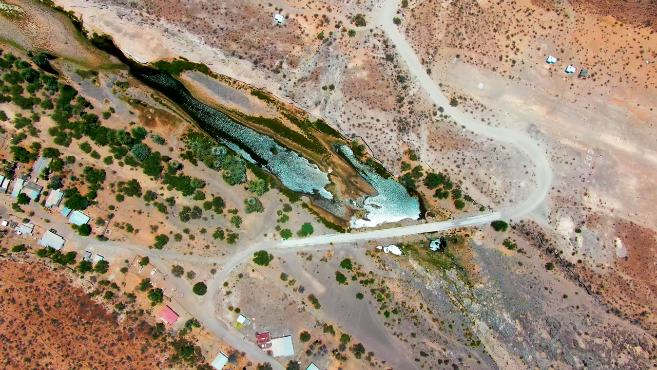 Aerial view of a narrow water channel beside desert scrub and a curving dirt road.
