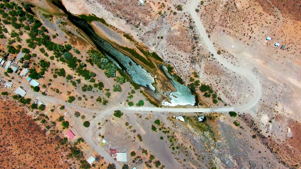 Aerial view of flowing water beside a dirt road crossing in arid land.