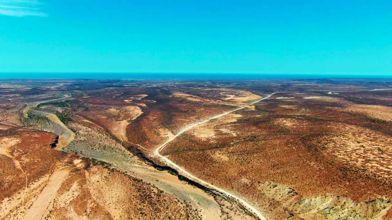 Third frame holds a high view of San Juanico desert terrain, where the winding river sits left of center, pale tracks cut across the midground, and no visible people appear in the open landscape.