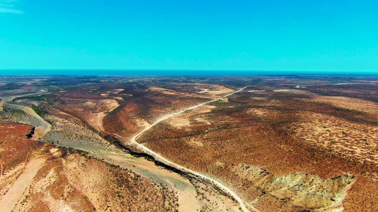Wide drone view of a winding dirt road and dry wash through red-brown desert.