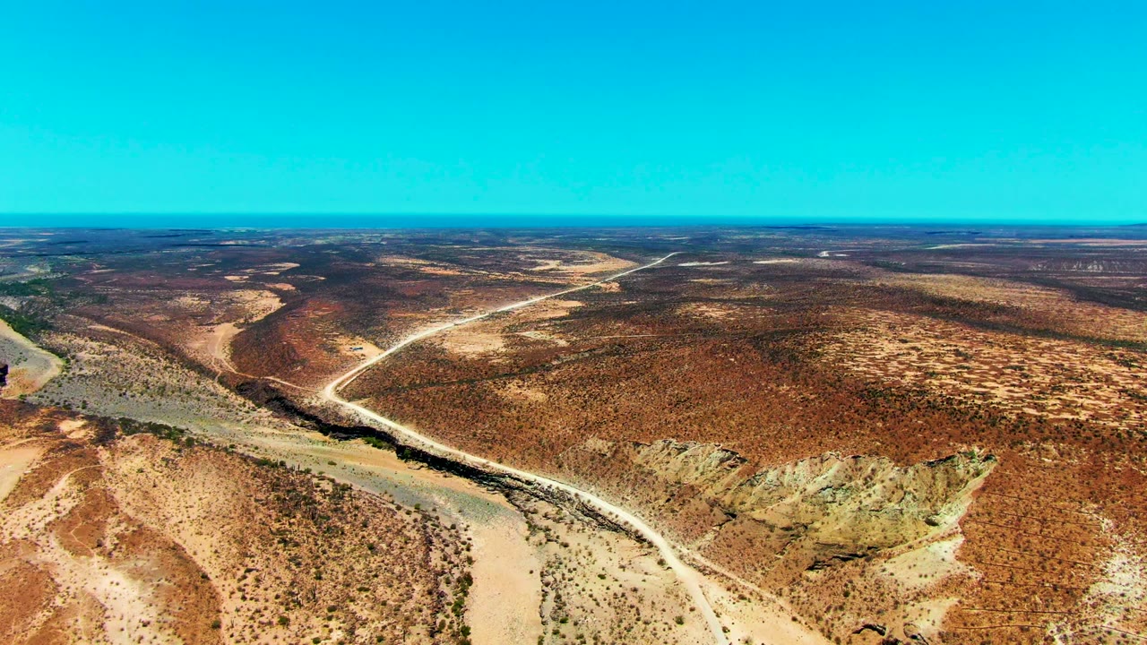 High desert landscape with pale road crossing scrub and a dry wash