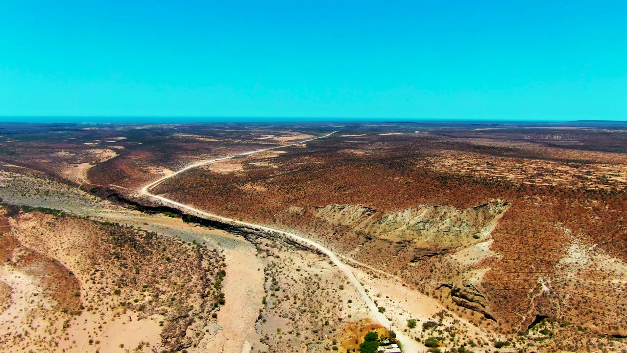 Aerial view of dry scrubland, rocky slopes, and a winding desert road.