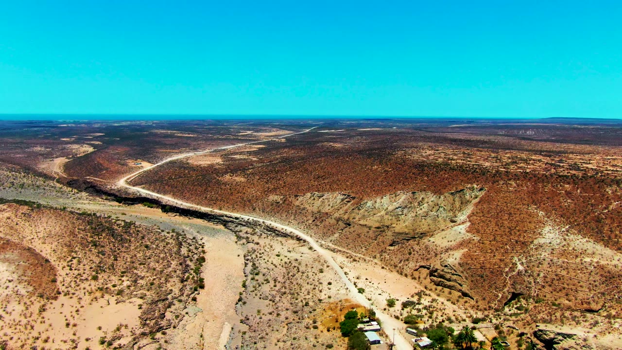 High desert landscape with a dirt road bending across scrub-covered hills.