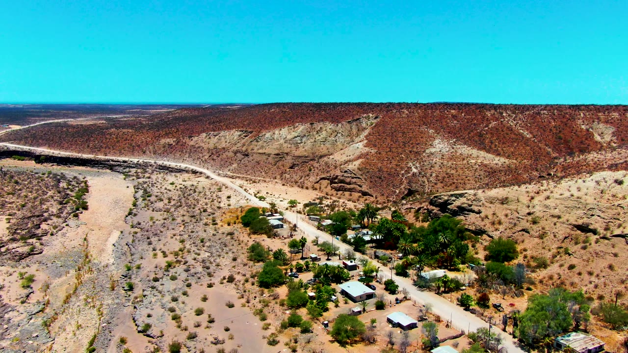 Elevated desert view with a dirt road crossing near trees and small roofs.