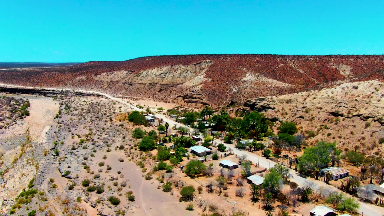 Drone view of a winding road beside desert buildings and rocky hills.