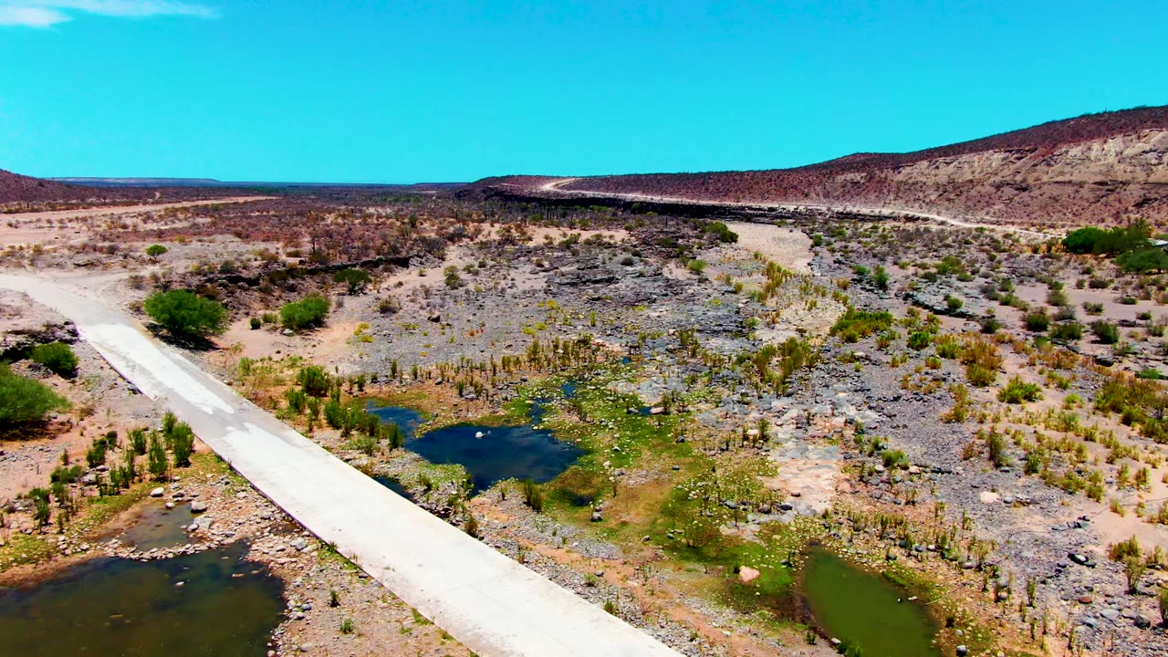 Bridge and water pools seen from above in dry rocky terrain.