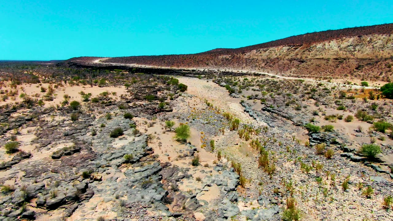Aerial view of a winding desert path bordered by rocks, scrub, and a long ridge.