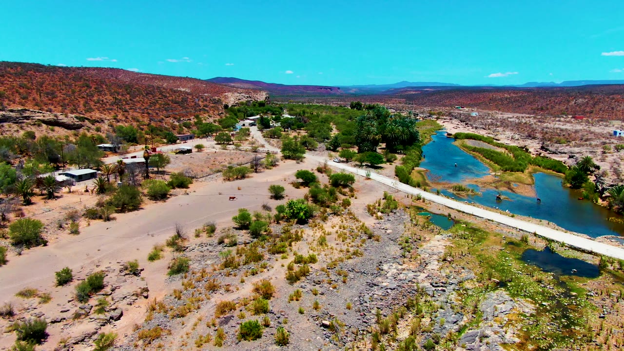 Drone view looking over a bridge crossing a river in dry desert terrain.