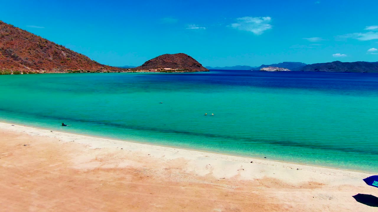 Turquoise bay beside a sandy beach with hills beyond.
