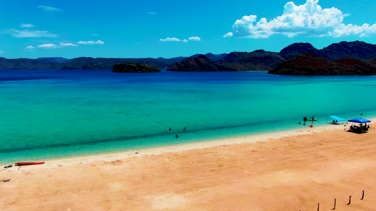 Wide aerial beach view with swimmers in turquoise water and a red boat on the sand