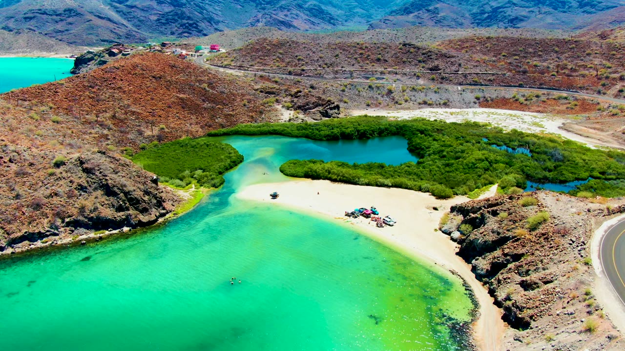Drone view of a sandy beach between turquoise water and green mangroves.