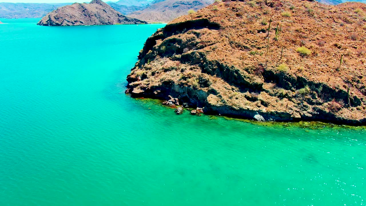 Rocky coastline with turquoise water and distant hills.