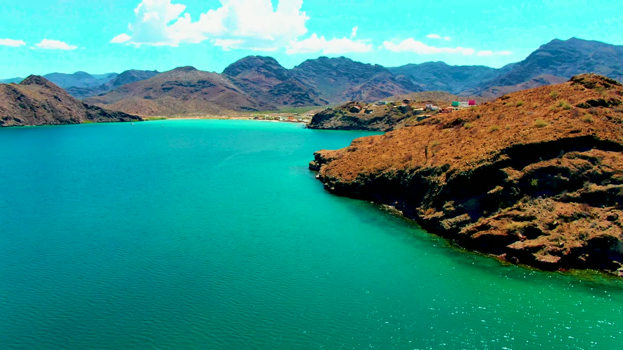 Aerial view of turquoise bay water, rocky shore, and distant mountains.