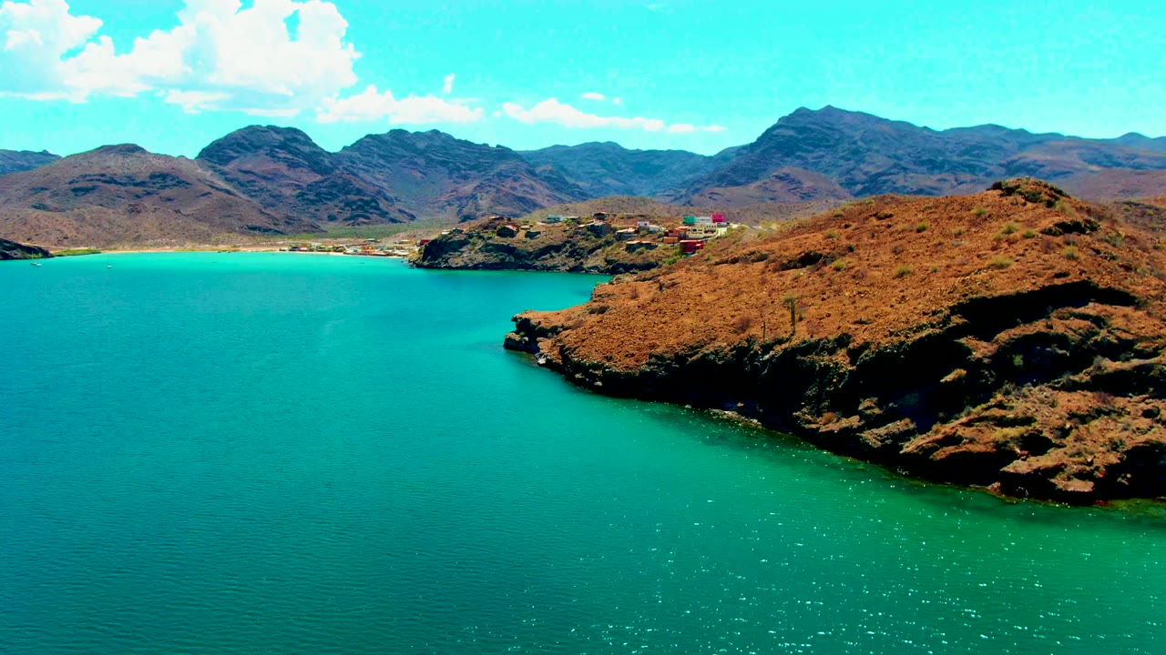 Wide coastal view with turquoise bay, rocky shore, and mountains.