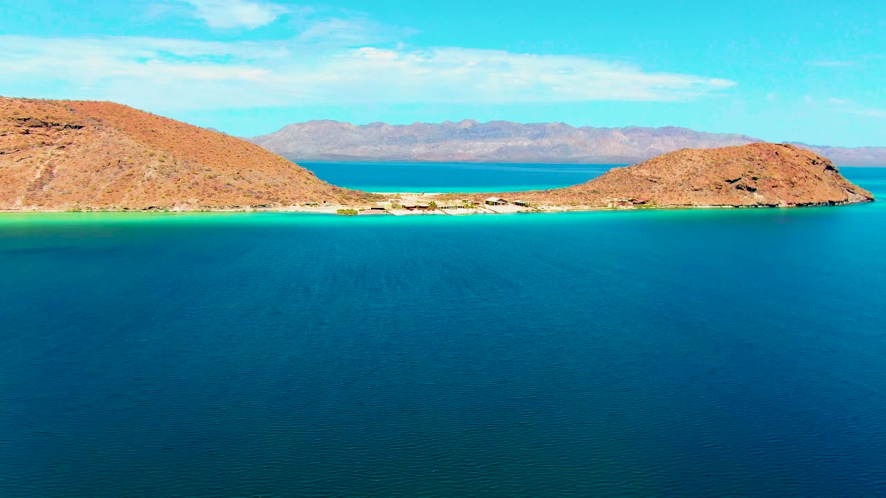 Turquoise shoreline channel with rocky islands and distant mountains.