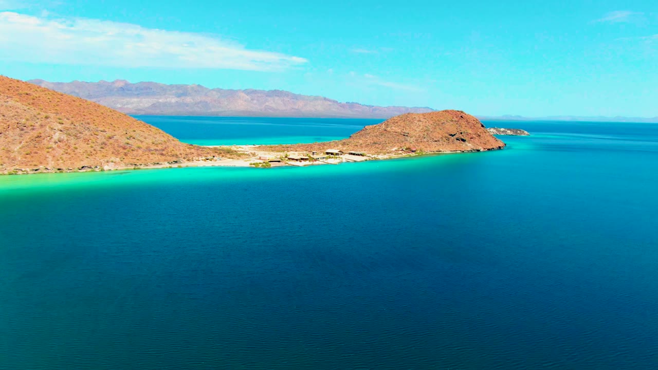 Wide aerial view of blue ocean, bright shallows, sandy beach, and tan hills.