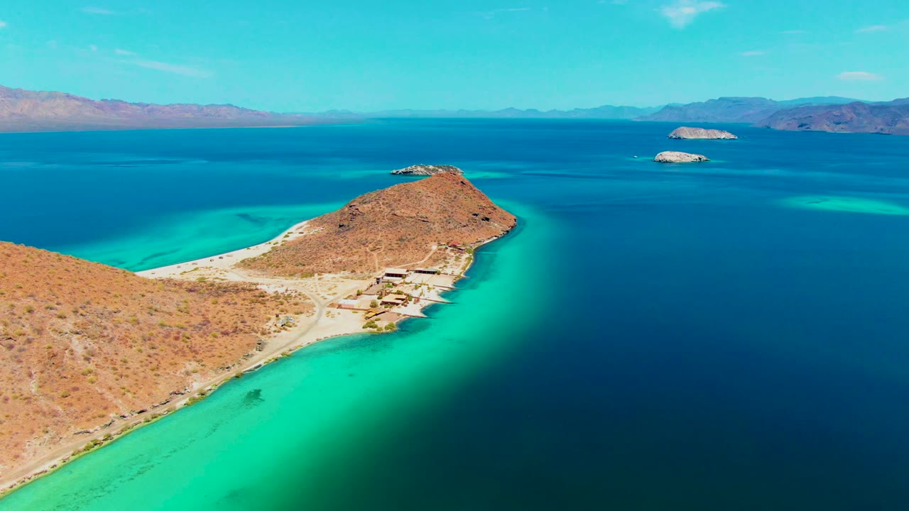 Rocky peninsula with bright turquoise shallows and distant islands under clear sky.