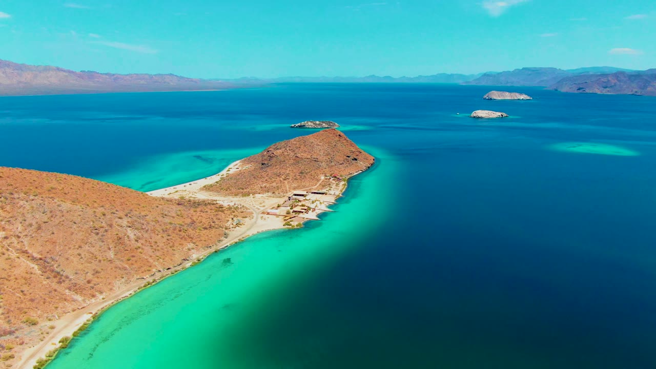 Desert shoreline and curved turquoise shallows with islands beyond.