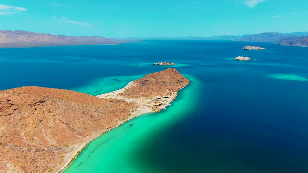 Desert shoreline curves into clear turquoise water with islands beyond.