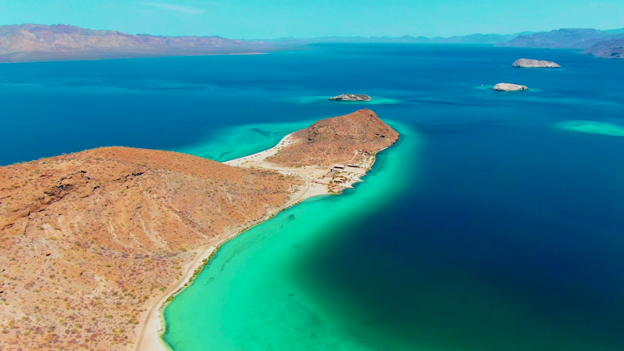 Rocky shoreline curves around bright turquoise water with islands offshore.