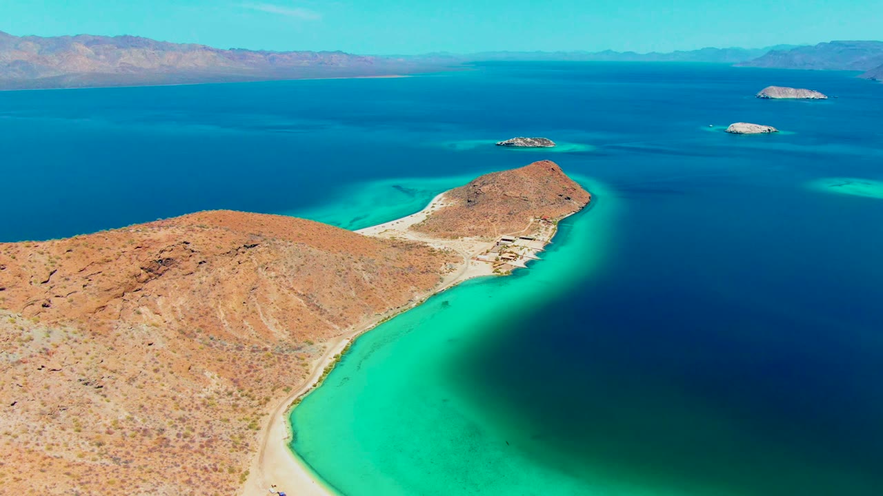 Desert shoreline curves around clear turquoise shallows with islands offshore.