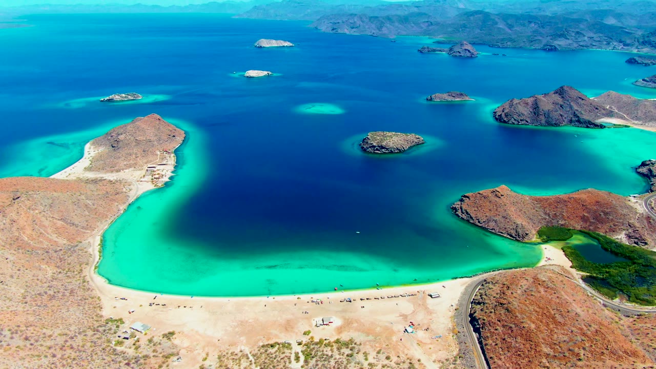 Wide aerial lagoon view with turquoise shallows, sandy beach, and rocky islands.