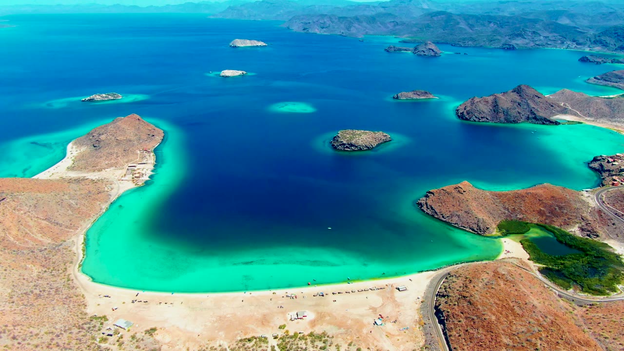 Wide drone view of sandy shore, turquoise water, islands, and dry coastal land.