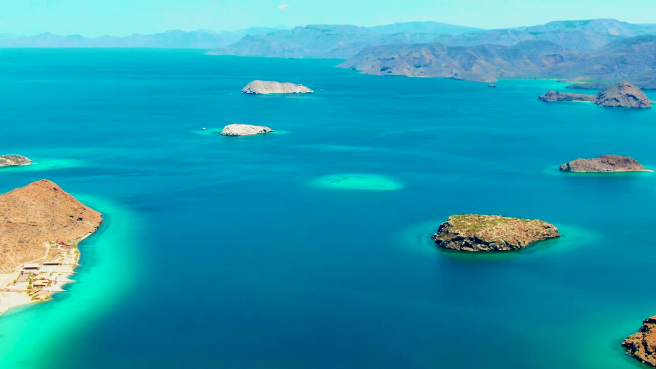 Wide drone view of small rocky islands and bright turquoise shallows.