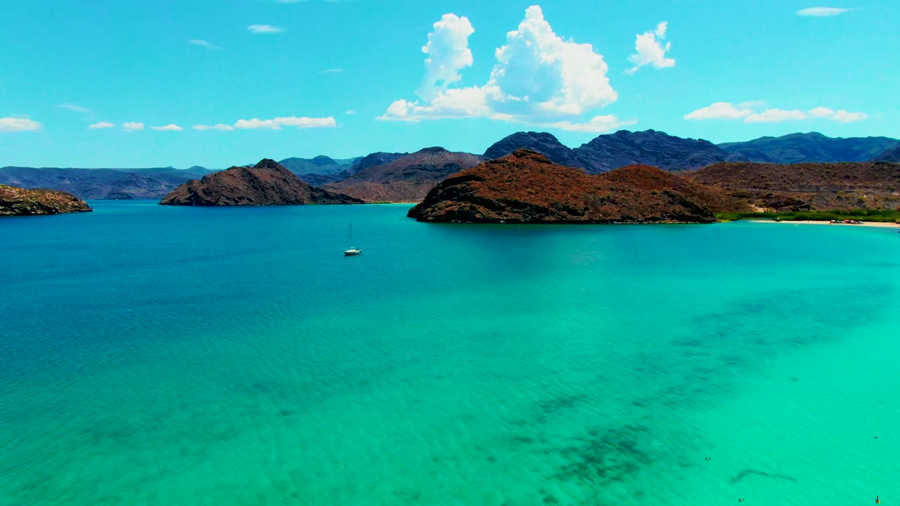 Small sailboat on clear turquoise water below rugged islands